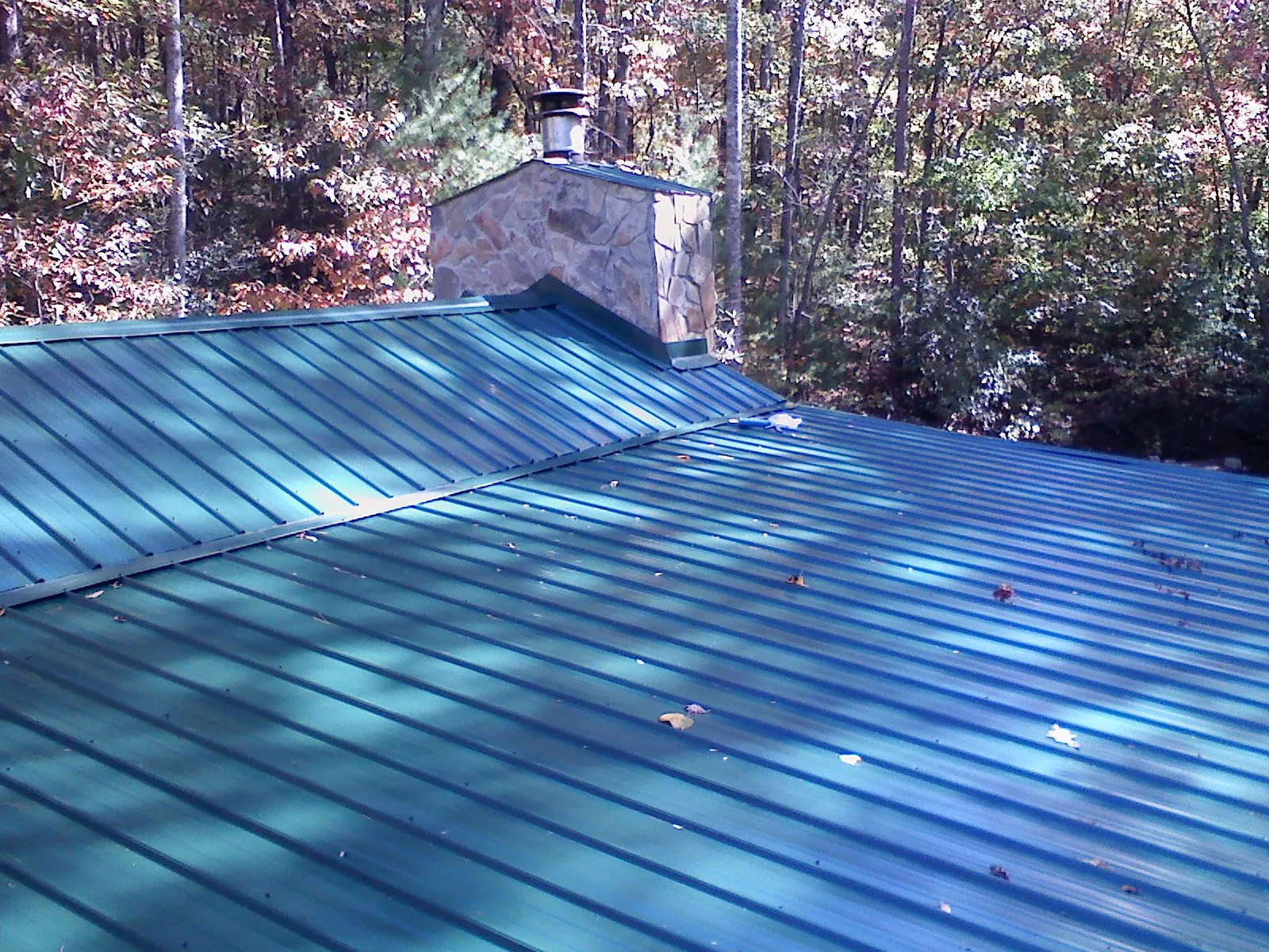New green metal roof and stone chimney surrounded by autumn woods in Lyons